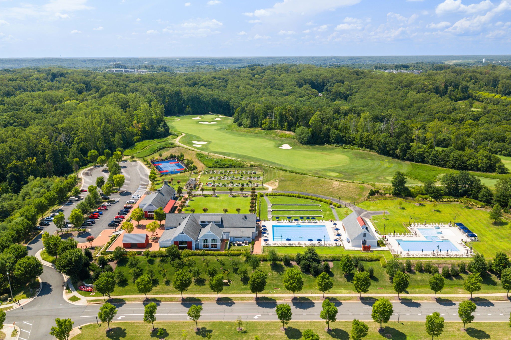 Wide aerial view of a clubhouse complex with pools, sport court, and golf course
