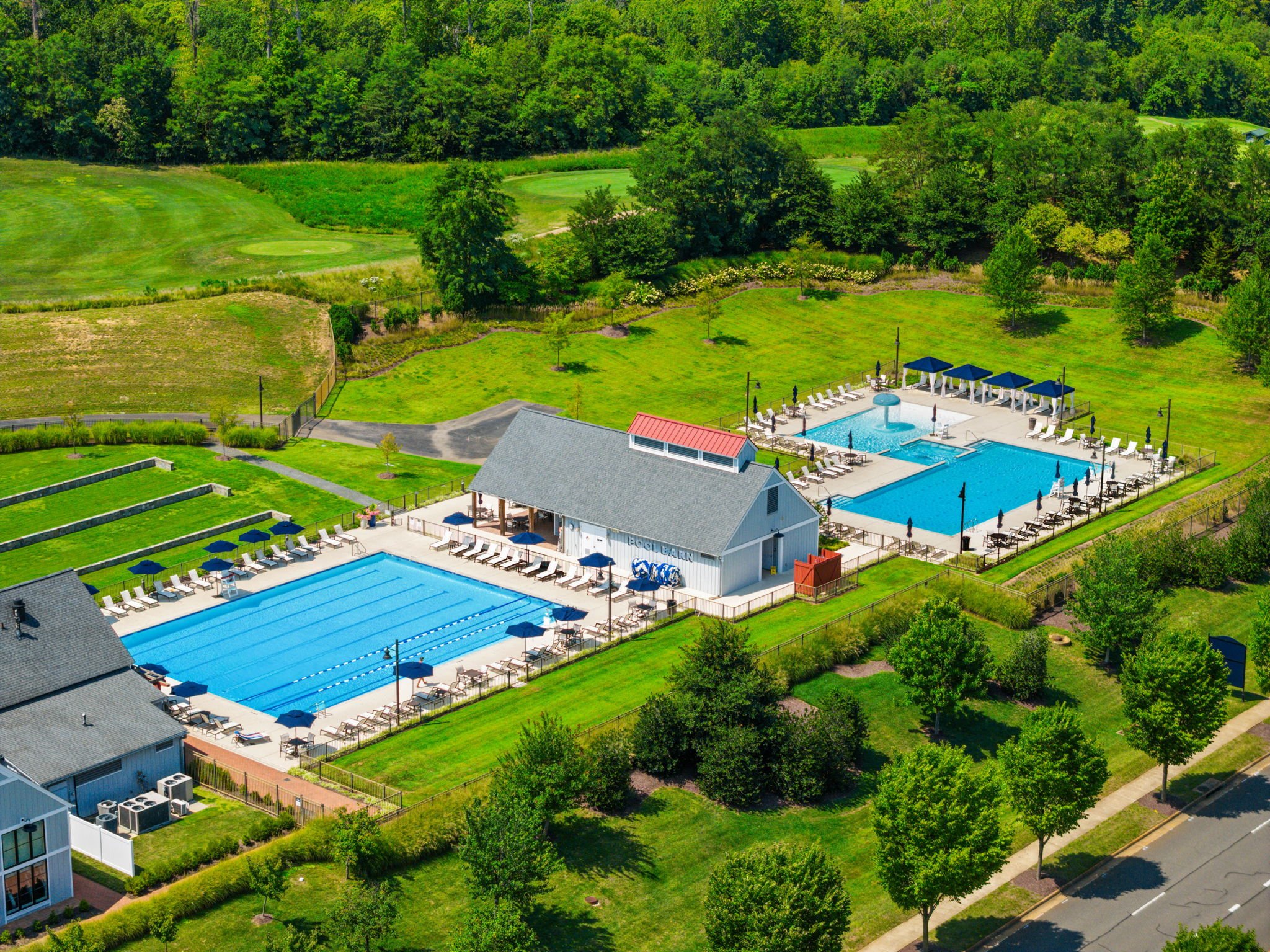 Aerial view of a pool barn clubhouse with two pools and golf course beyond