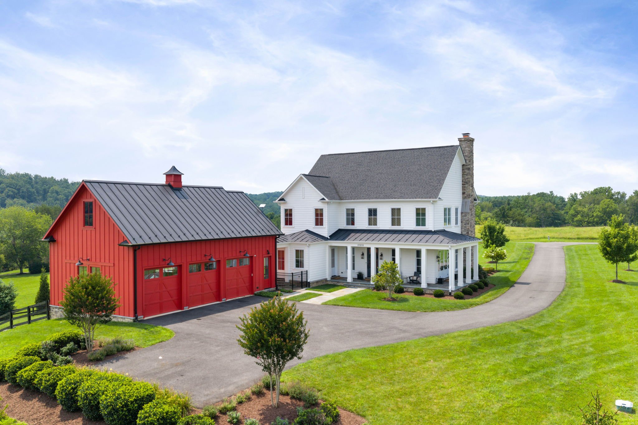 Aerial view of a white farmhouse with matching red barn along a winding driveway