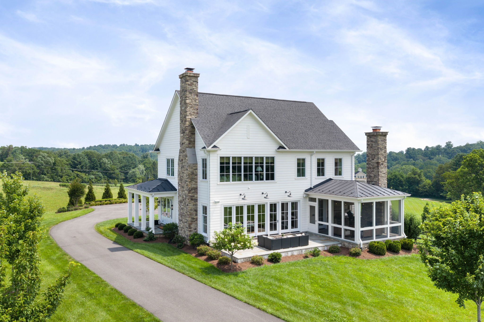 Aerial view of a white farmhouse's rear exterior with stone chimneys and screened porch