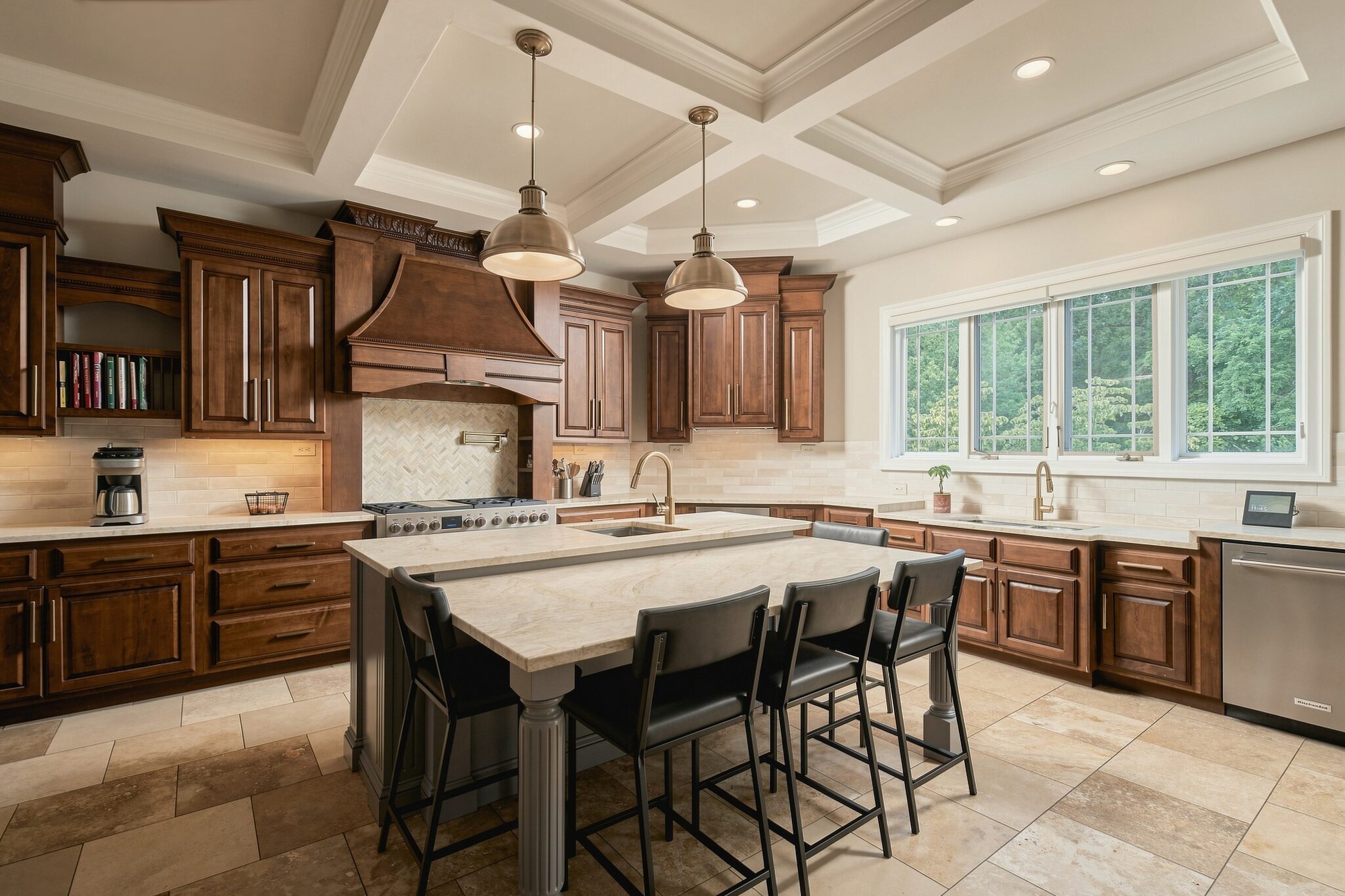 Kitchen island with black stools beneath a carved wood range hood and brass pendant lights