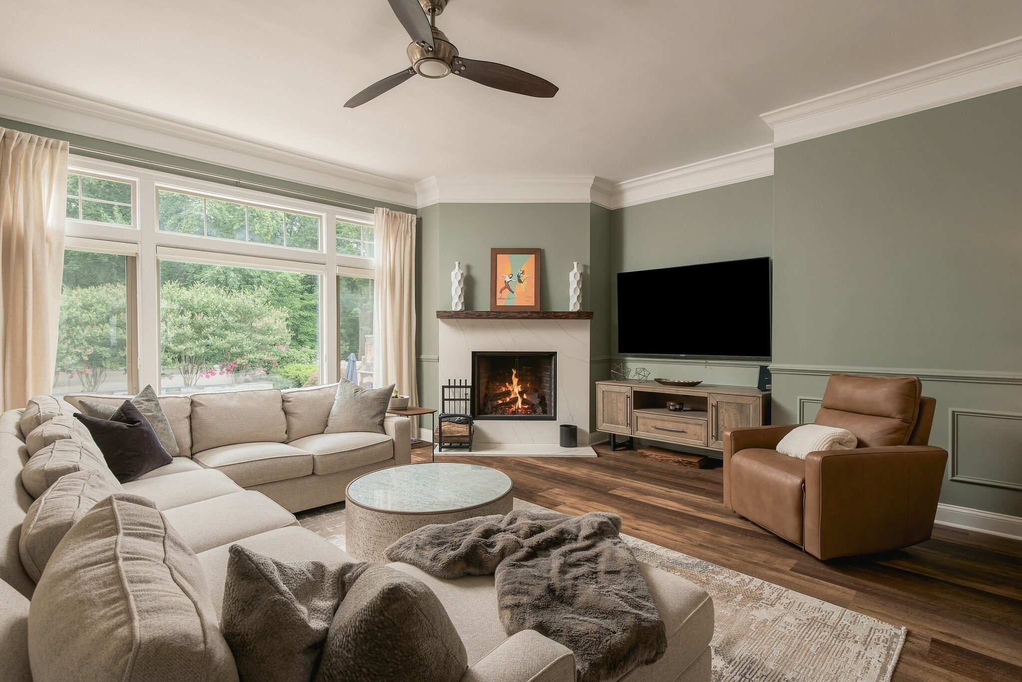 Spacious living room with sectional sofa, stone fireplace, and wall-mounted TV under a ceiling fan