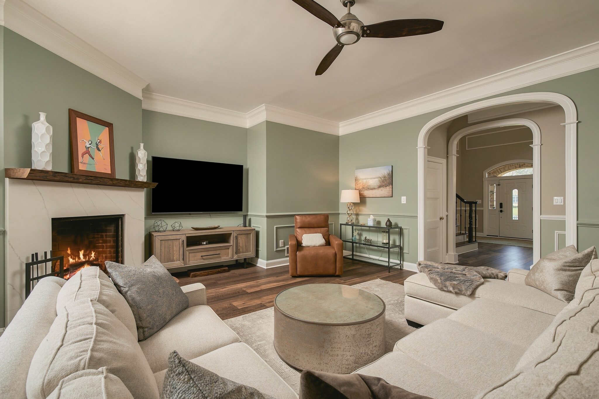 Living room fireplace and TV wall with leather recliner and archway to the foyer and staircase
